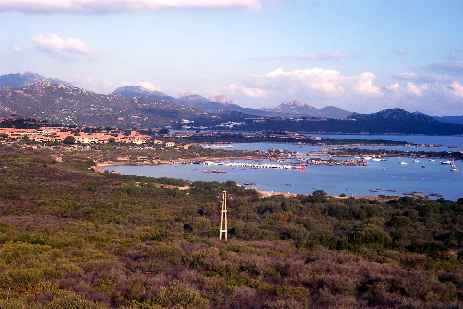Il golfo di Marinella dall'alto, con le case affacciate sulla baia, le barche ormeggiate e i monti della Gallura sullo sfondo